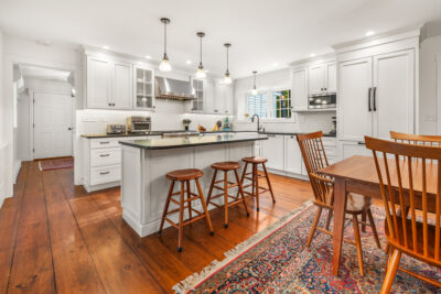 Open kitchen with central island, dining area, and fireplace in Quechee Colonial home